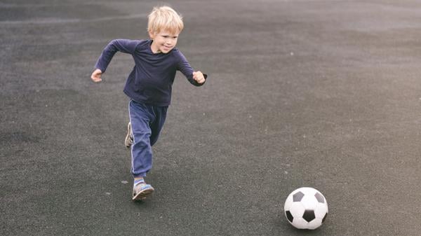 Ein Kind mit kurzen blonden Haaren läuft auf einen Fußball zu. 
