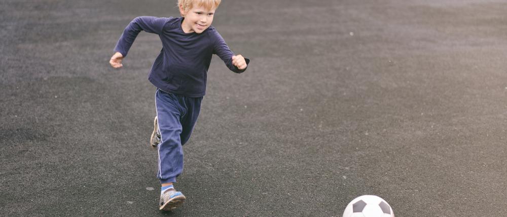 Ein Kind mit kurzen blonden Haaren läuft auf einen Fußball zu.
