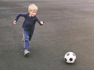 Ein Kind mit kurzen blonden Haaren läuft auf einen Fußball zu. 