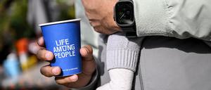 PRODUKTION - 25.09.2025, Berlin: Ein junger Mann hält einen Kaffeebecher der LAP-Kaffeekette in der Hand während er ein Baby auf dem Arm hat. (zu dpa: «Günstiger Kaffee im Trend - LAP Coffee fordert Szene heraus») Foto: Britta Pedersen/dpa +++ dpa-Bildfunk +++