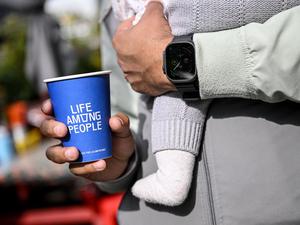 PRODUKTION - 25.09.2025, Berlin: Ein junger Mann hält einen Kaffeebecher der LAP-Kaffeekette in der Hand während er ein Baby auf dem Arm hat. (zu dpa: «Günstiger Kaffee im Trend - LAP Coffee fordert Szene heraus») Foto: Britta Pedersen/dpa +++ dpa-Bildfunk +++