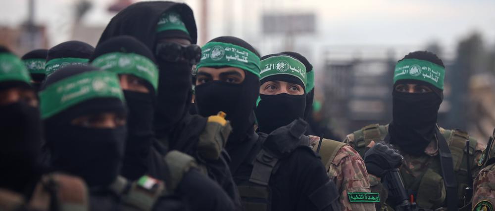 Hamas-Kämpfer stehen in Formation, während sich Palästinenser auf einer Straße versammeln (Symbolbild).