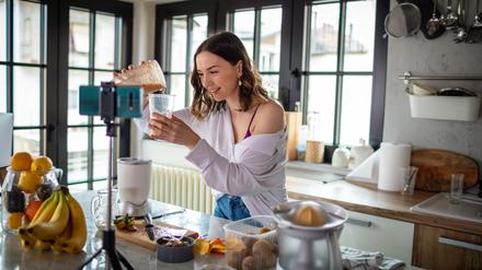 Eine junge Frau bereitet Essen vor einer Kamera zu.