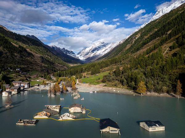 30.09.2025, Schweiz, Blatten: Ein Luftbild zeigt die zerstörten und überfluteten Häuser im Dorf Blatten, 4 Monate nachdem ein Erdrutsch das Dorf zerstört hat. Am 28. Mai 2025 wurde das Dorf Blatten im Lötschental, Kanton Wallis, verwüstet, als ein Teil des Birkengletschers einbrach und eine Lawine aus Fels, Eis und Geröll ins Lötschental schickte. Etwa 90 % des Dorfes, darunter 130 Häuser und die Pfarrkirche, wurden verschüttet. Die Trümmer blockierten den Fluss Lonza, wodurch ein großer See entstand und Überschwemmungen zu befürchten waren. Die Behörden in Blatten hatten das Dorf bereits in der Woche vor dem Gletscherabbruch evakuiert, wobei ein örtlicher Hirte ums Leben kam. (KEYSTONE/Michael Buholzer) Foto: Michael Buholzer/KEYSTONE/dpa +++ dpa-Bildfunk +++