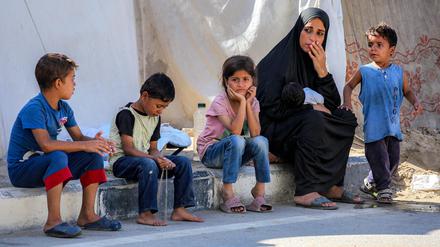 Eine Frau sitzt mit Kindern vor Zelten in einem Lager für Kriegsflüchtlinge im nördlichen Nuseirat im zentralen Gazastreifen.