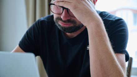 Ein Mann sitzt vor einem Laptop und seufzt.