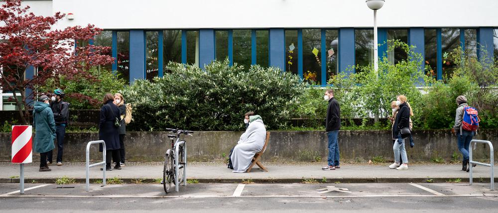 14.05.2021, Berlin: Maikel Fritz und Mia Faustmann (M) aus Neukölln warten auf Klappstühlen sitzend auf dem Gehweg vor einer Turnhalle einer Schule in Neukölln, wo eine Schwerpunktimpfung gegen Corona stattfindet. Bei dem gemeinsamen Pilotprojekt des Senats und des Bezirksamts Neukölln sind Anwohner festgelegter Straßen in einem Viertel mit hoher Inzidenz eingeladen, eine Corona-Impfung ohne Termin zu erhalten. Geimpft wird mit den Impfstoffen der Firmen Johnson & Johnson sowie Moderna. Foto: Bernd von Jutrczenka/dpa +++ dpa-Bildfunk +++