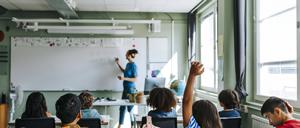Eine Lehrerin an der Tafel in einem vollen Klassenraum.