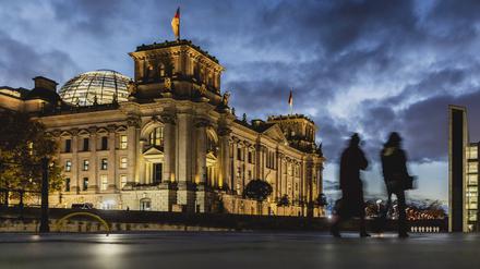 Zwei Personen zeichnen sich ab vor dem Deutschen Bundestag bei blauer Stunde in Berlin. 