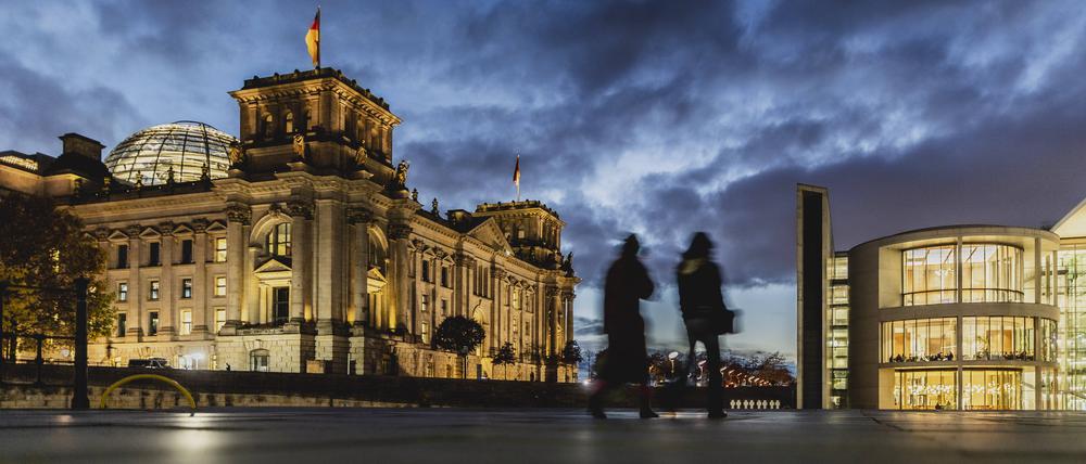 Zwei Personen zeichnen sich ab vor dem Deutschen Bundestag bei blauer Stunde in Berlin.