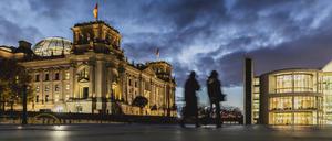 Zwei Personen zeichnen sich ab vor dem Deutschen Bundestag bei blauer Stunde in Berlin. 