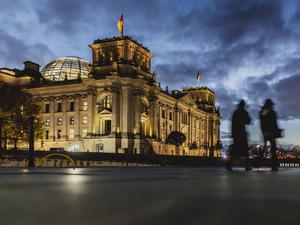 Zwei Personen zeichnen sich ab vor dem Deutschen Bundestag bei blauer Stunde in Berlin. 