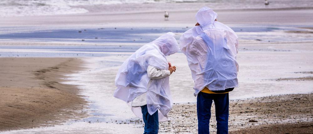 Spaziergänger mit Regenschutz suchen bei kräftigem Wind am Ostseestrand von Warnemünde nach Bernstein (Symbolbild).