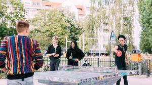 Mehrere junge Menschen spielen Tischtennis in einem Park.