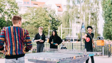 Mehrere junge Menschen spielen Tischtennis in einem Park.