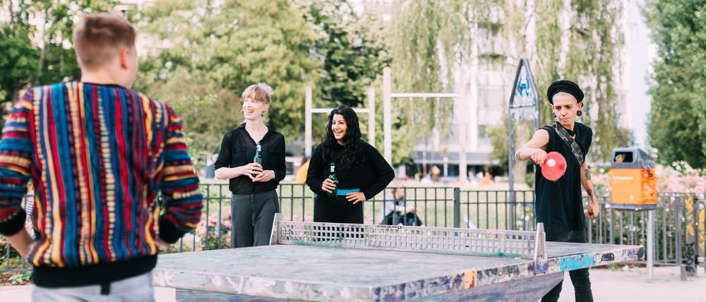 Mehrere junge Menschen spielen Tischtennis in einem Park.