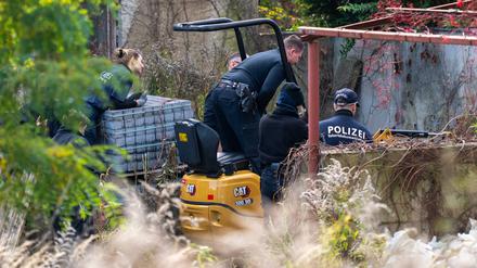 Polizisten untersuchen mit einem Bagger ein Grundstück in Tauche.