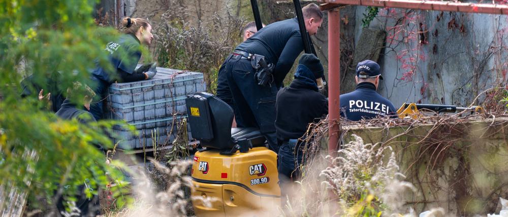 Polizisten untersuchen mit einem Bagger ein Grundstück in Tauche.
