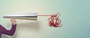 Eine Hand mit einem Megafon und einem Drahtknäuel (Illustration).