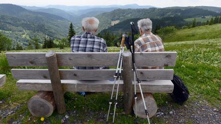 Zwei ältere Wanderer im Schwarzwald ruhen sich auf einer Bank aus.