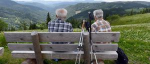 Zwei ältere Wanderer im Schwarzwald ruhen sich auf einer Bank aus.  