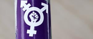 Ein Aufkleber einer Faust inmitten der drei Geschlechter ist auf lila Grund zu sehen.