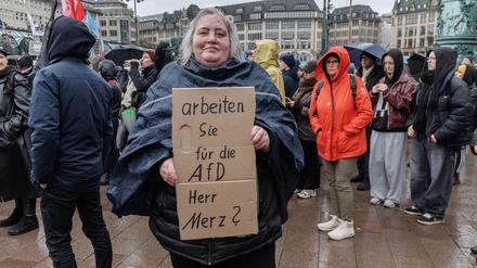 Eine Demonstrantin in Hamburg stellt auf einem Pappschild eine Frage an Bundeskanzler Friedrich Merz (CDU).