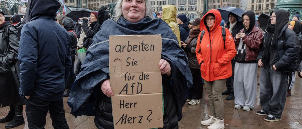 Eine Demonstrantin in Hamburg stellt auf einem Pappschild eine Frage an Bundeskanzler Friedrich Merz (CDU). 