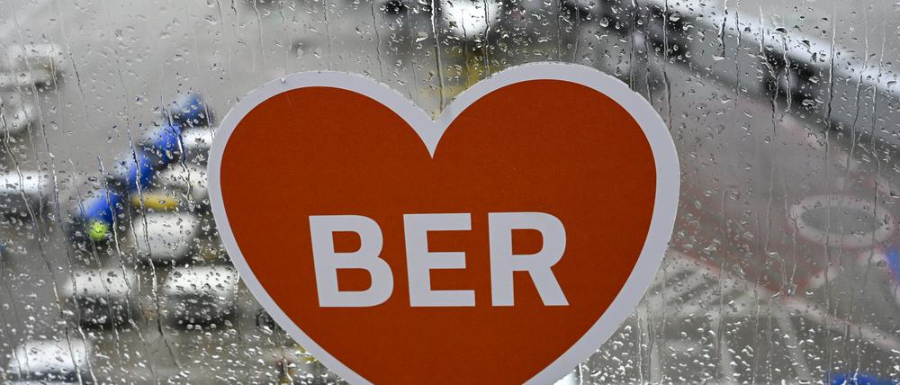Ein Aufkleber mit einem Herz und den Buchstaben BER ist auf der Besucherterrasse am Flughafen BER bei Regenwetter vor einem Flugzeug zu sehen. 