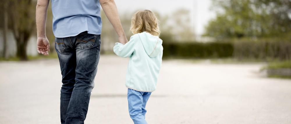 Ein Kind geht an der Hand eines Mannes.