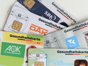 Gesundheitskarten verschiedener Krankenkassen liegen auf einem Tisch.