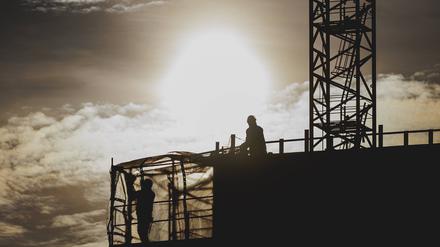 Zwei Bauarbeiter zeichnen sich ab als Silhouette vor der untergehenden Sonne - wird der neue Bauturbo den Wohnungsbau in Berlin beschleunigen?