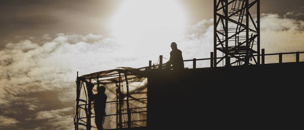Zwei Bauarbeiter zeichnen sich ab als Silhouette vor der untergehenden Sonne - wird der neue Bauturbo den Wohnungsbau in Berlin beschleunigen?