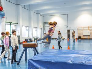 Kinder beim Bocksprung in einer Turnhalle.