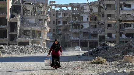 Eine Frau geht inmitten vieler zerstörter Häuser in Damaskus eine Straße entlang.