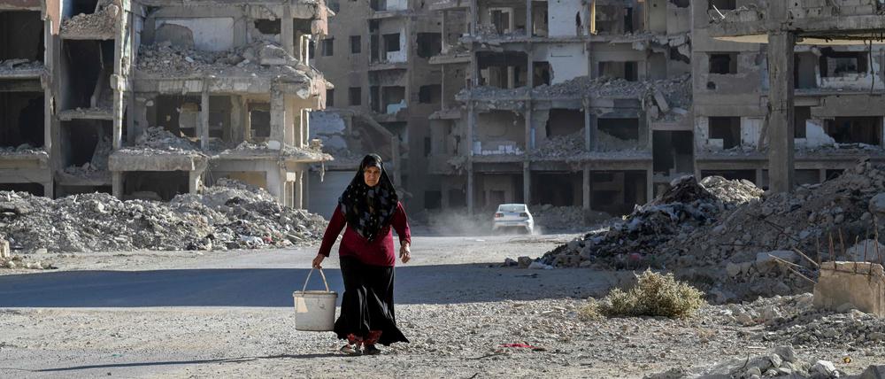 Eine Frau geht inmitten vieler zerstörter Häuser in Damaskus eine Straße entlang.