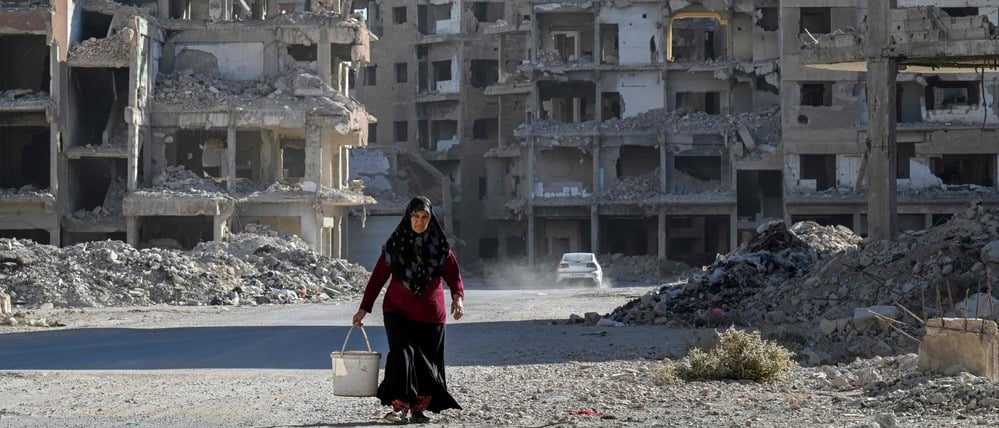 Eine Frau geht inmitten vieler zerstörter Häuser in Damaskus eine Straße entlang.