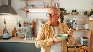 Ein älterer Mann ist im Stehen in seiner Küche ein Müsli.