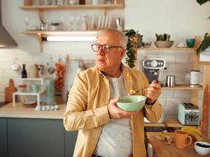 Ein älterer Mann ist im Stehen in seiner Küche ein Müsli.