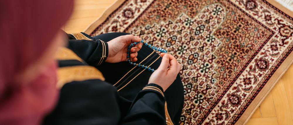 Eine Person ist von oben betend auf einem Teppich zu sehen. (Symbolbild)