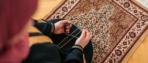 Beautiful young Muslim woman praying using prayer beads (misbaha,tasbih) and a prayer mat at home. Close-up.