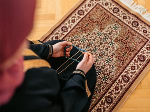 Eine Person ist von oben betend auf einem Teppich zu sehen. (Symbolbild)