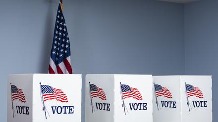 Wahlurnen vor einer US-Flagge.