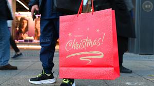 Ein Mann steht mit einer weihnachtlichen Verkaufstüte mit dem Spruch „Merry Christmas“ am Kurfürstendamm in Berlin. 