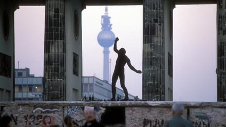 Eine Person tanzt auf der Mauer am Brandenburger Tor.