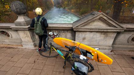 Ein Mann mit einem Surfboard an seinem Fahrrad schaut von einer Brücke auf die - nicht mehr vorhandene - Eisbachwelle im Englischen Garten.