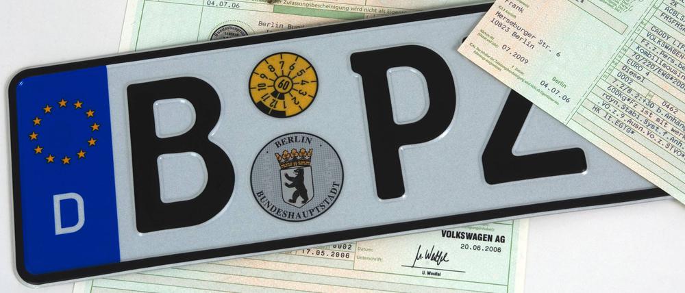 Ein Symbolbild zeigt ein Berliner Autokennzeichen, einen Autoschlüssel und einen Fahrzeugbrief. 