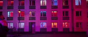 Freier vor der Fassade eines rot beleuchteten Bordells mit Prostituierten in den Fenstern in Düsseldorf.
