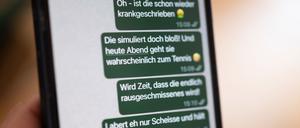 Eine Person hält ein Smartphone in der Hand, auf dessen Bildschirm beleidigende Nachrichten in einem Chat zu sehen sind (gestellte Szene).