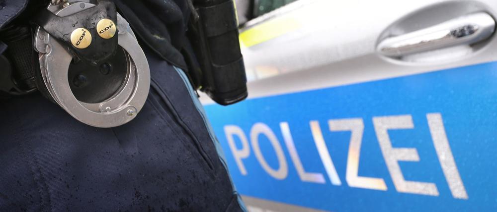 Ein Polizist mit Handschellen und einer Pistole am Gürtel steht vor einem Streifenwagen.